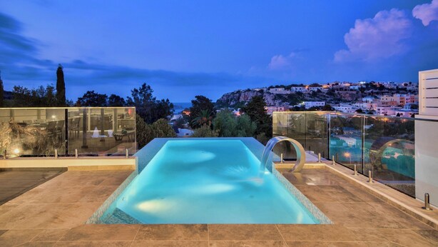 Une piscine sur le toit offrant une vue dégagée sur une ville perchée sur une colline, au crépuscule.