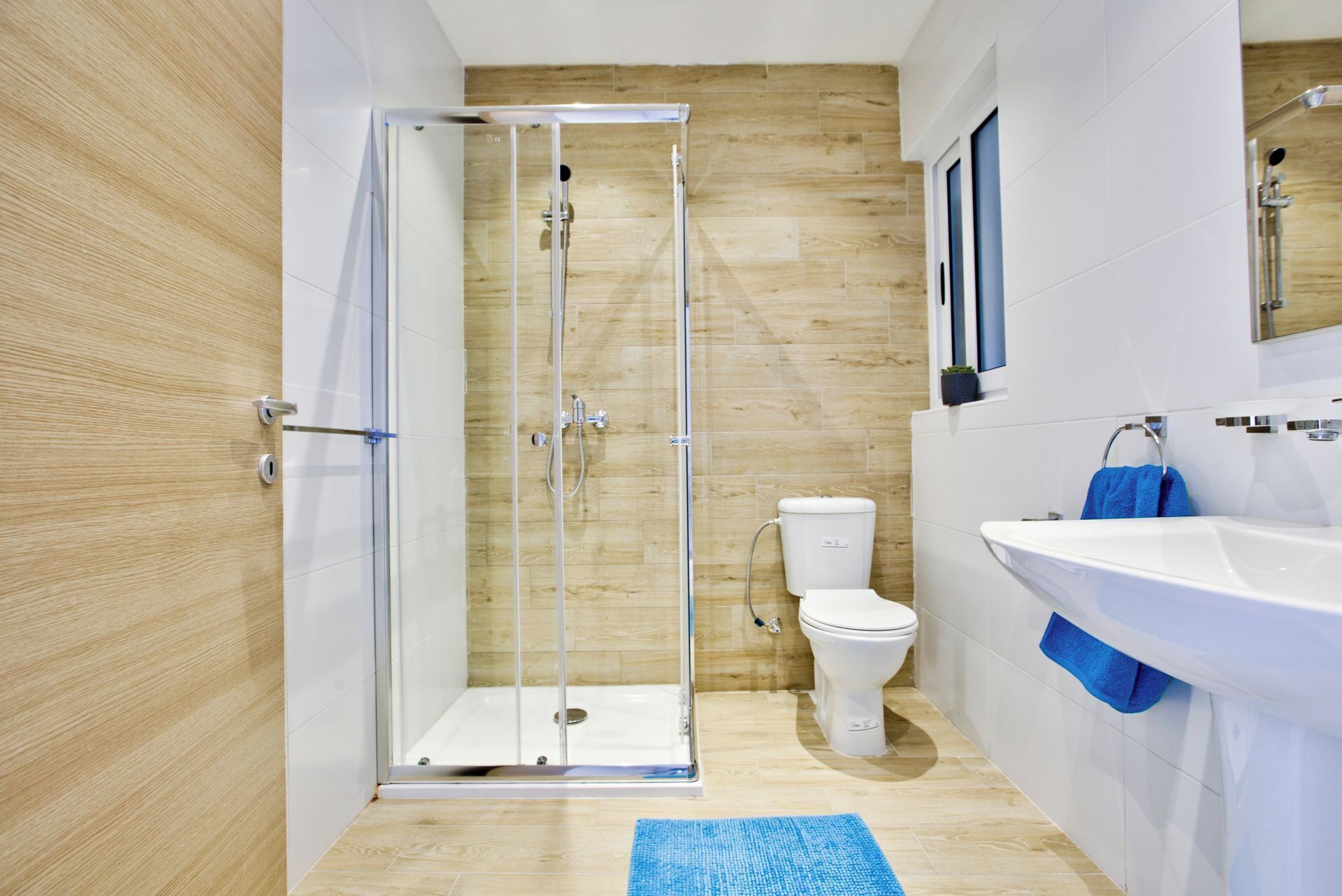 A modern bathroom with a glass-enclosed shower, a white toilet, and a sink with a blue towel.