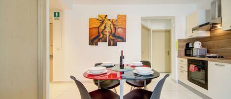 A modern dining area with a table set for four, a wine bottle, and abstract art on the wall.