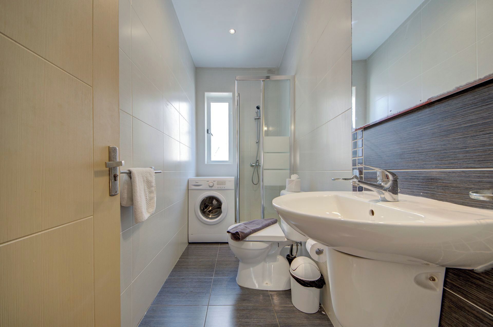 A modern bathroom with a washing machine, toilet, sink, and glass shower enclosure.