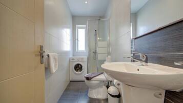 A modern bathroom with a washing machine, toilet, sink, and glass shower enclosure.