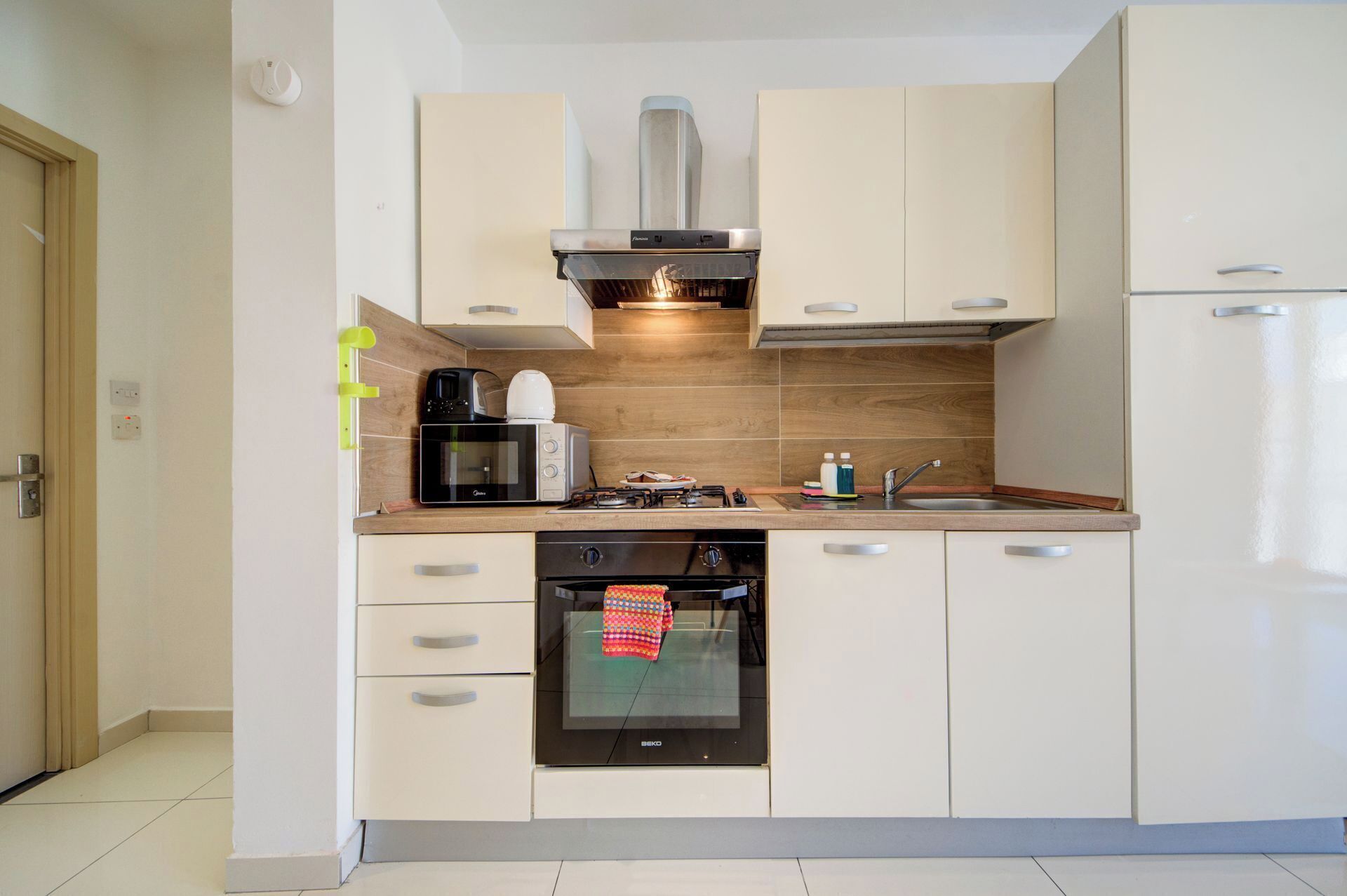 Une cuisine moderne avec des meubles blancs, un four encastré, un four à micro-ondes, une machine à café et une cuisinière à gaz.