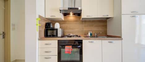 Une cuisine moderne avec des meubles blancs, un four encastré, un four à micro-ondes, une machine à café et une cuisinière à gaz.
