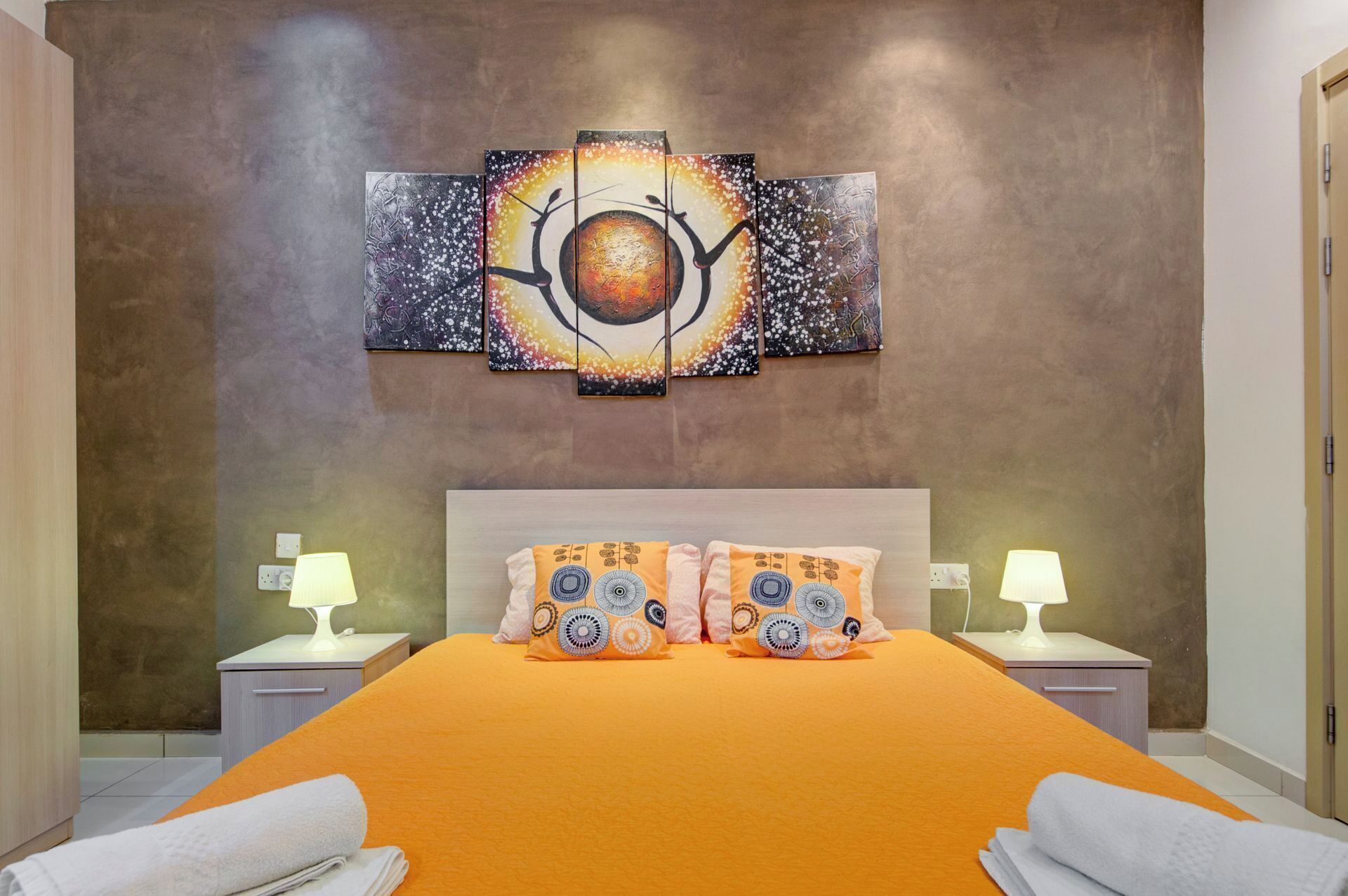 A hotel room with a large bed, two nightstands, and a wall-mounted artwork.