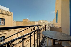 A balcony with a table and chairs, overlooking a cityscape with buildings and a clear sky. - Exclusive Holiday Flat Steps to the Sliema Shops (Sliema)