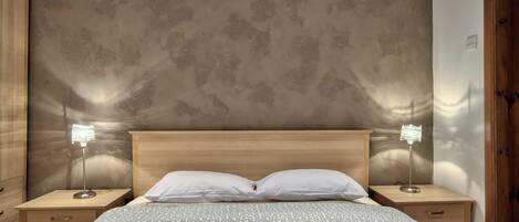 A bedroom with a wooden headboard, two bedside tables with lamps, a patterned bedspread, and a textured wall.