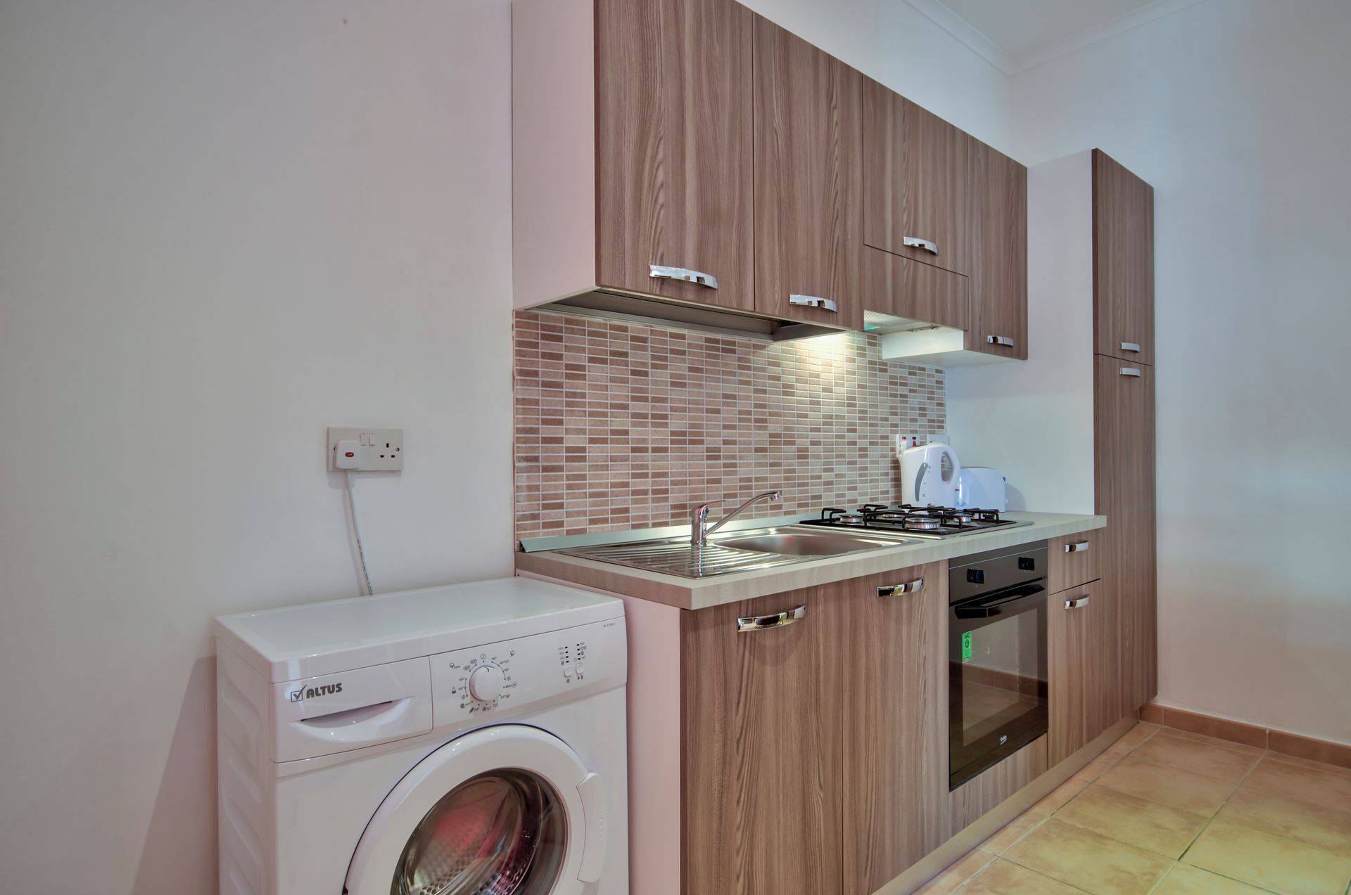 Una cucina compatta con mobili in legno, forno a incasso, piano cottura a gas e lavatrice.