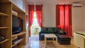 A living room with a sofa, coffee table, TV, and a wooden shelf with a telephone. - Delightful Apartment With Traditional Balcony (Sliema)