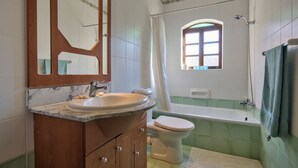 A bathroom with a marble sink, wooden cabinets, a toilet, a bathtub, and a window with a view. - Delightful Apartment With Traditional Balcony (Sliema)