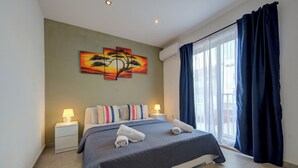 A hotel room with a bed, two bedside tables, a painting on the wall, and a large window with curtains. - Stunning Penthouse Apartment With Private Terrace (Gzira)