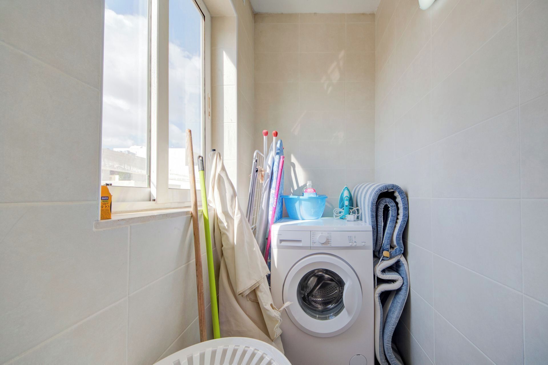 A small laundry room with a washing machine, ironing board, and cleaning supplies.