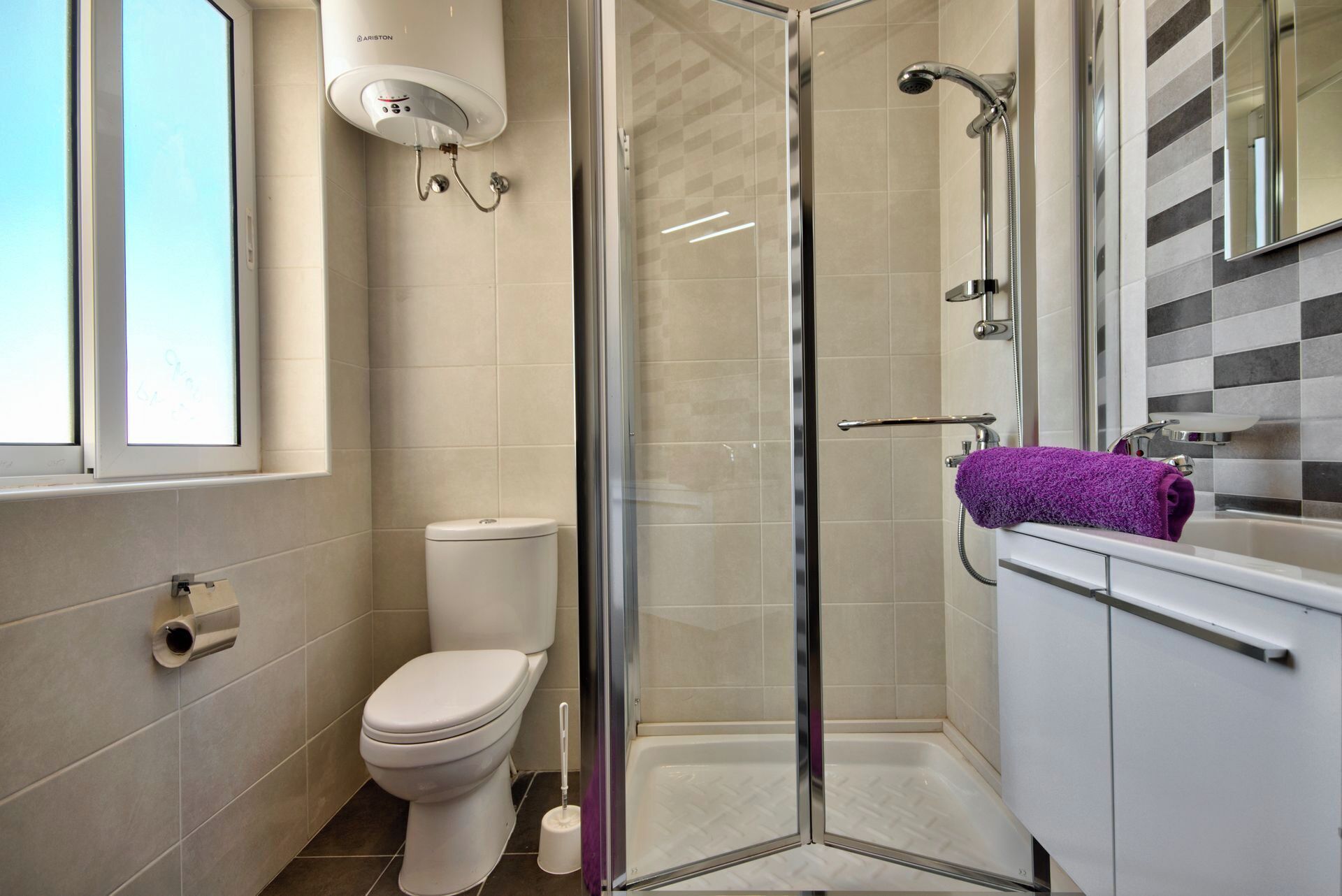 A modern bathroom with a glass-enclosed shower, a toilet, and a sink with a purple towel.