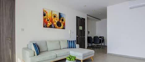 A modern living room with a light-colored sectional sofa, a small coffee table with a plant, and a large painting of sunflowers on the wall.