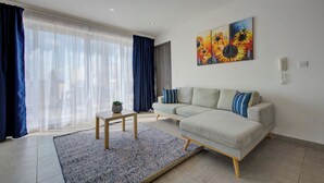 A modern living room with a sofa, a coffee table, and a rug. There is a painting of sunflowers on the wall. - Stunning Penthouse Apartment With Private Terrace (Gzira)