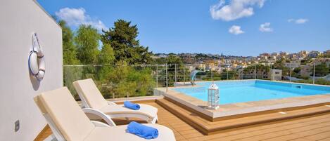 A rooftop pool area with lounge chairs and a view of a town.