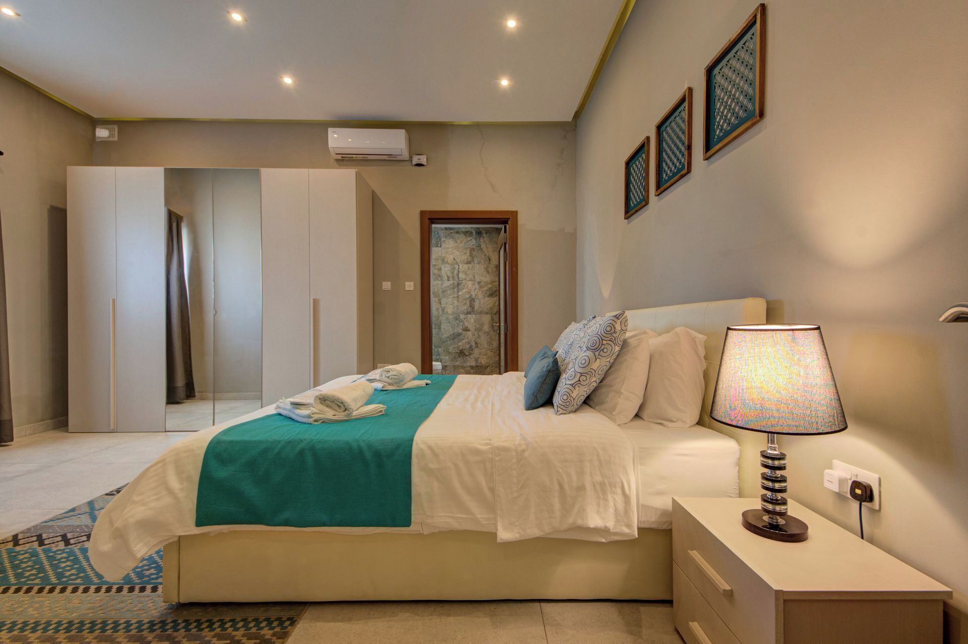 Habitación de hotel con cama, mesita de noche, lámpara y puerta que da a un baño.