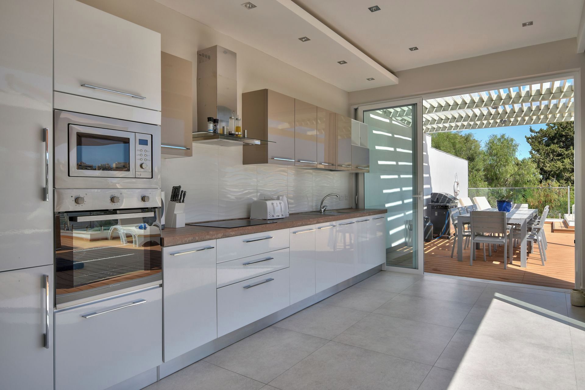 Una cocina moderna con armarios blancos, horno integrado y un amplio ventanal con vistas a un patio.