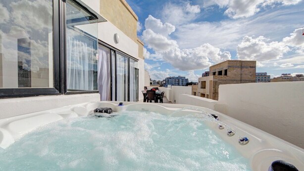 Ein Whirlpool auf dem Dach mit Glasverkleidung, einem Tisch und Stühlen und Blick auf die Skyline.