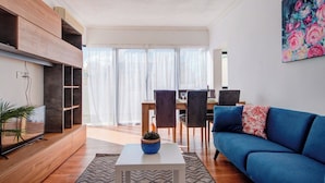 Ein modernes Wohnzimmer mit einem blauen Sofa, einem weißen Couchtisch und einem Essbereich mit Stühlen und Tisch.