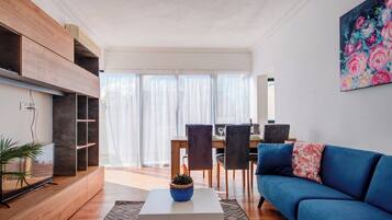 Uma sala de estar moderna com um sofá azul, uma mesa de centro branca e uma área de jantar com cadeiras e uma mesa.