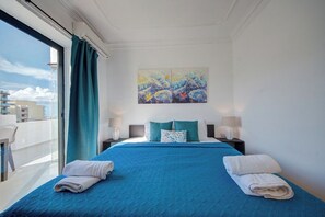 Ein Hotelzimmer mit einem großen Bett, zwei Nachttischen, einem Bild an der Wand und Blick auf Gebäude durch ein Fenster.