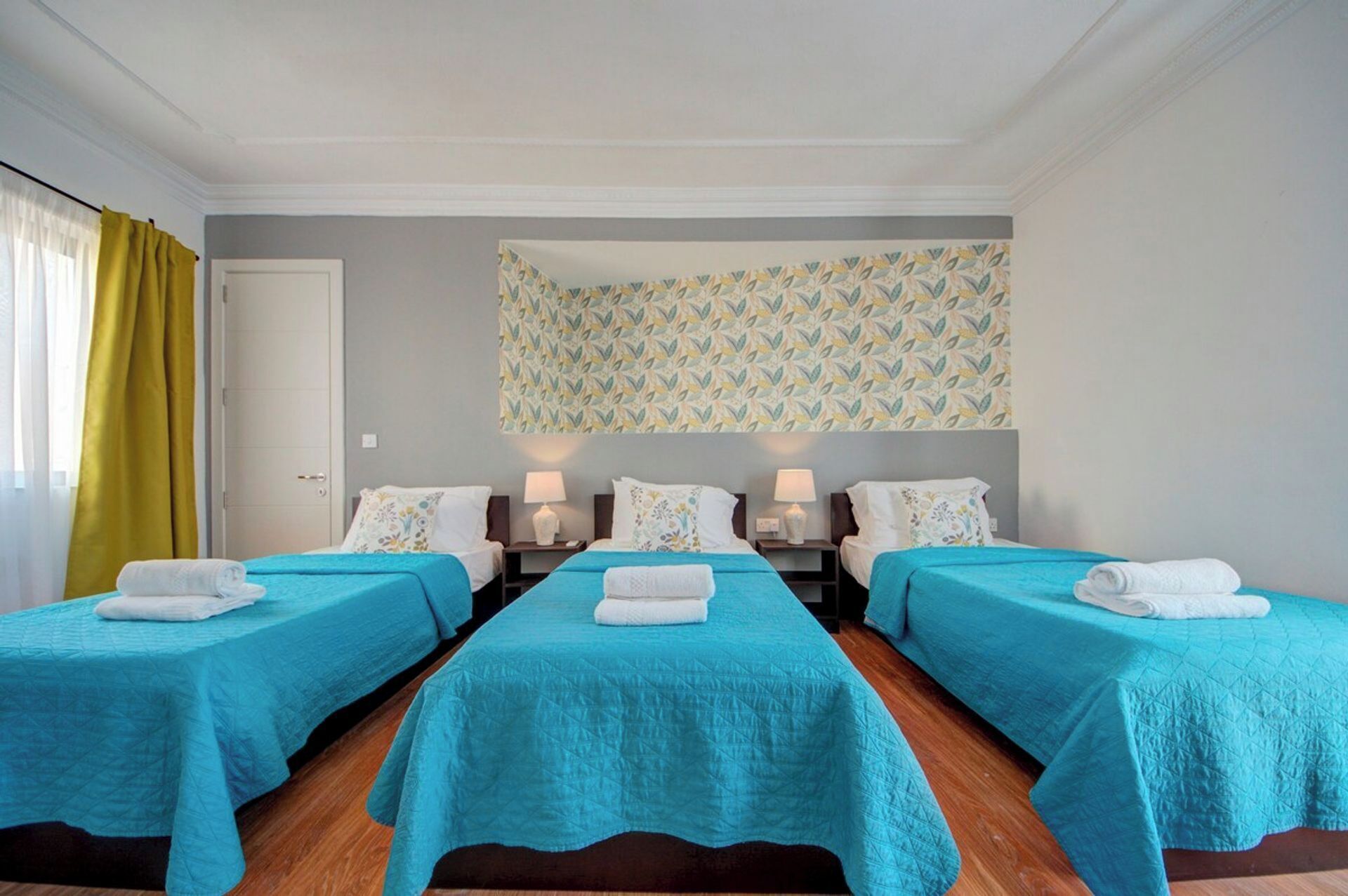 A hotel room with four single beds, each with a blue bedspread and white towels.