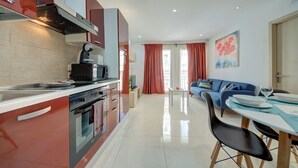 A modern kitchen with a microwave, toaster, and kettle, leading to a dining area with a blue sofa and a table set for two. - Off the Ferries, Sliema, 2-bedroom Apartment (Sliema)