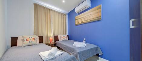 A hotel room with two beds, a painting on the wall, and an air conditioning unit.