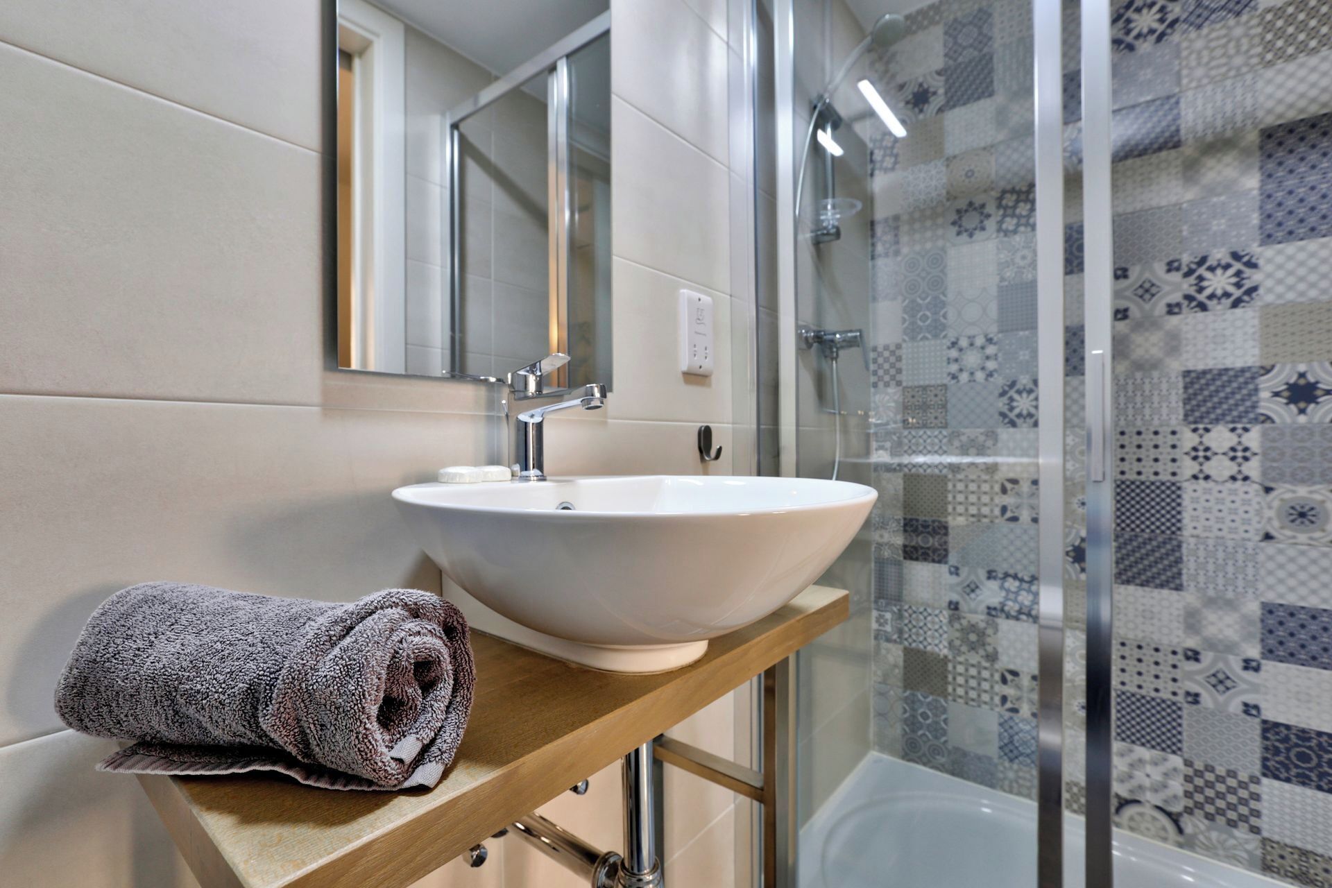 Un baño con un lavamanos blanco, un espejo y una ducha con azulejos estampados.