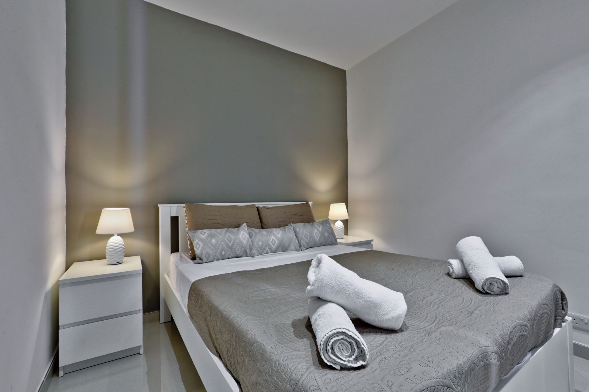 A modern bedroom with a large bed, two bedside tables with lamps, and neatly folded towels on the bed.
