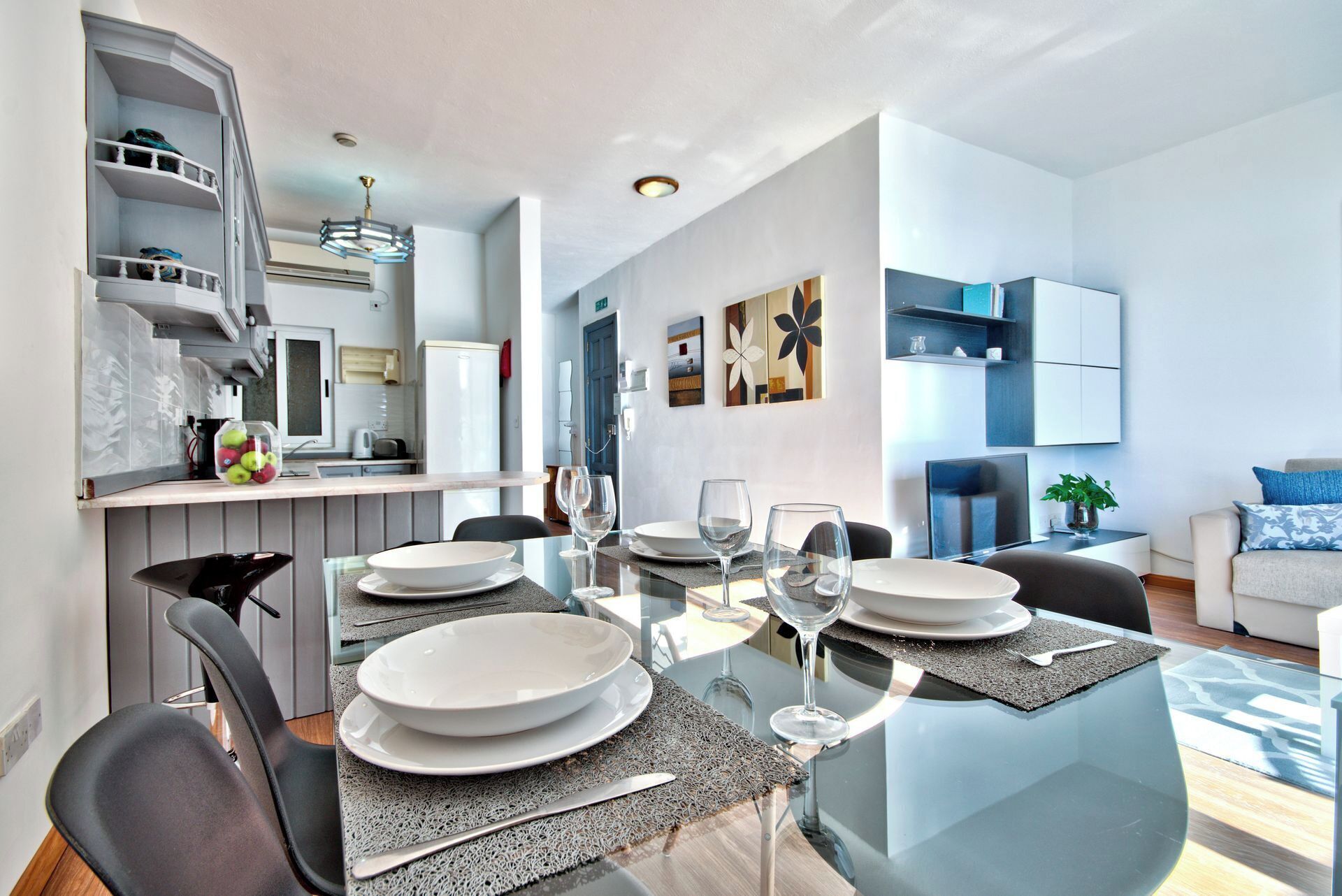A modern dining area with a glass table, white plates, and wine glasses set for four.