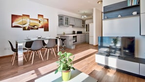 A modern kitchen with grey cabinets, a built-in oven, and a microwave. There is a dining area with a glass table and chairs, and a TV mounted on the wall. - Stunning Home Overlooking Valletta City Skyline (Sliema)