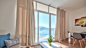 A modern living room with a sofa, a coffee table, and a dining area with a table and chairs. Large windows offer a view of the sea. - Stunning Home Overlooking Valletta City Skyline (Sliema)