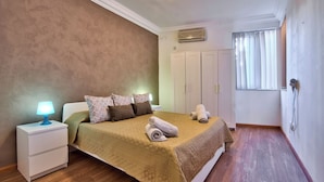 A bedroom with a bed, a nightstand with a lamp, a wardrobe, and a window with blinds. - Stunning Home Overlooking Valletta City Skyline (Sliema)