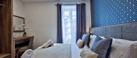 Habitación de hotel con cama, mesita de noche, espejo, ventana con cortinas y pared con diseño.