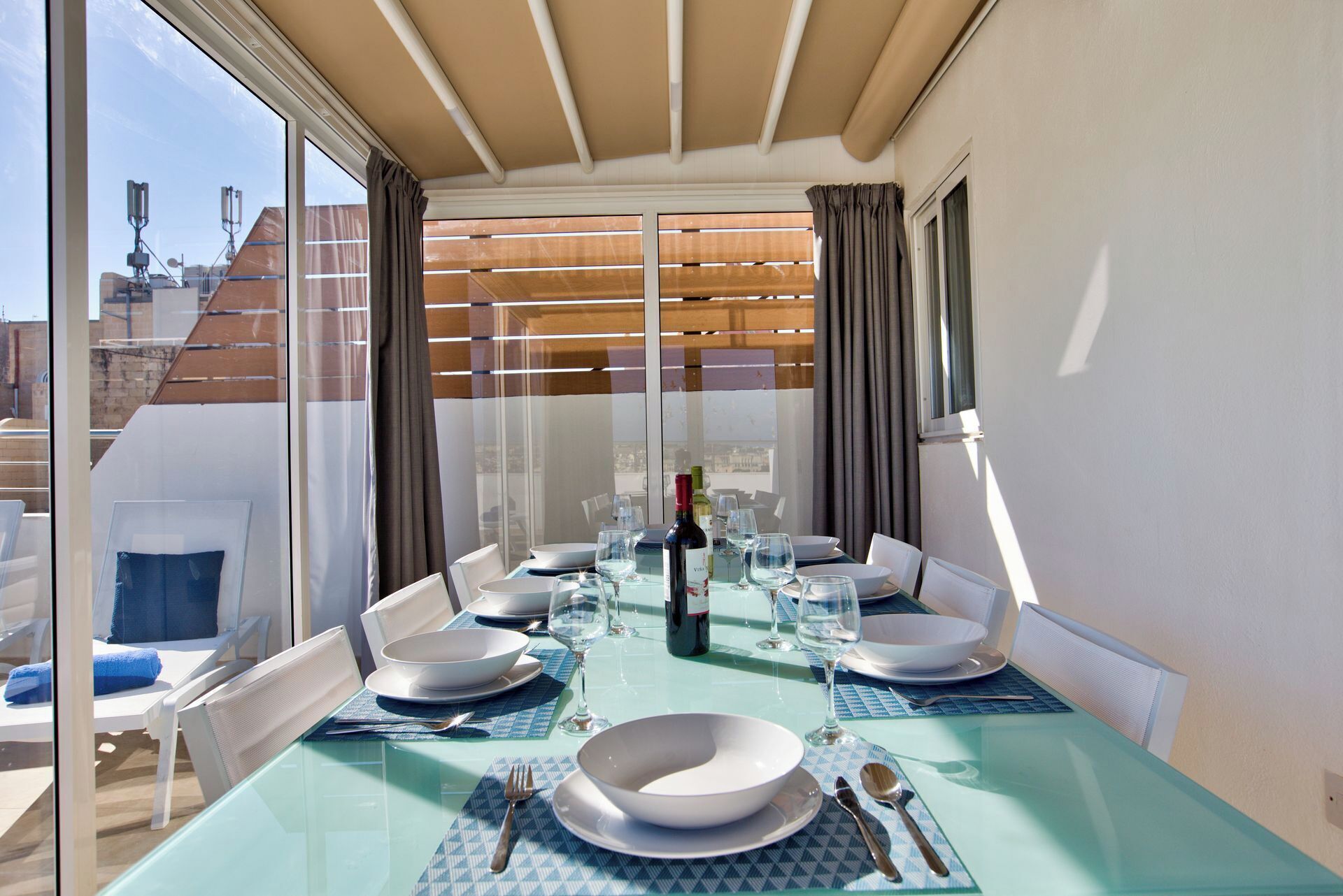 Un espace repas avec une table en verre, des chaises blanches et une vue sur le paysage urbain grâce à de grandes fenêtres.