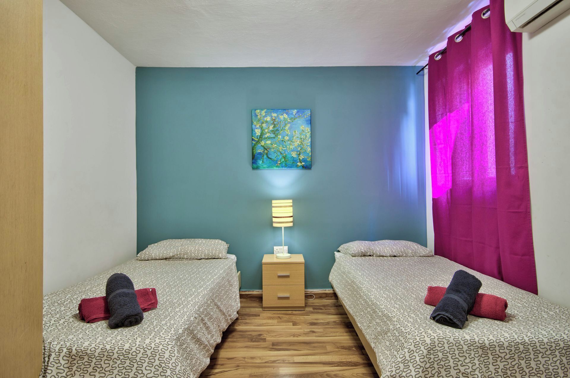 A room with two beds, a nightstand, a lamp, and a painting on the wall.