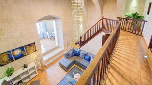 A spacious living area with a wooden staircase, a large sofa, and a view of the adjacent room. - Enchanting Stone Villa With Pool and Jacuzzi (Valletta)