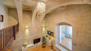 A spacious interior with a stone wall, a wooden staircase, a modern chandelier, and a television. - Enchanting Stone Villa With Pool and Jacuzzi (Valletta)