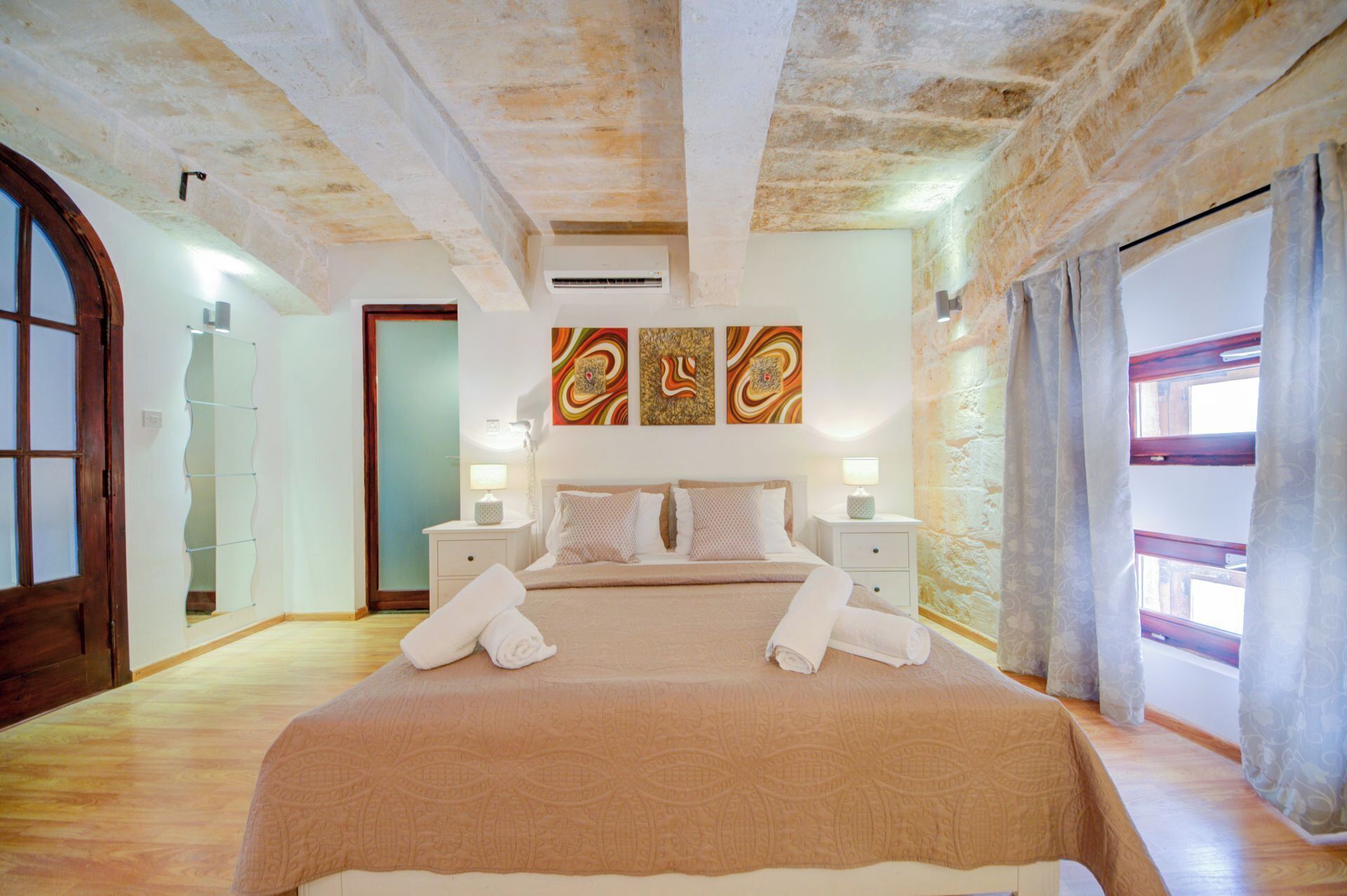 A bedroom with a large bed, two bedside tables, a mirror, and a window with curtains.