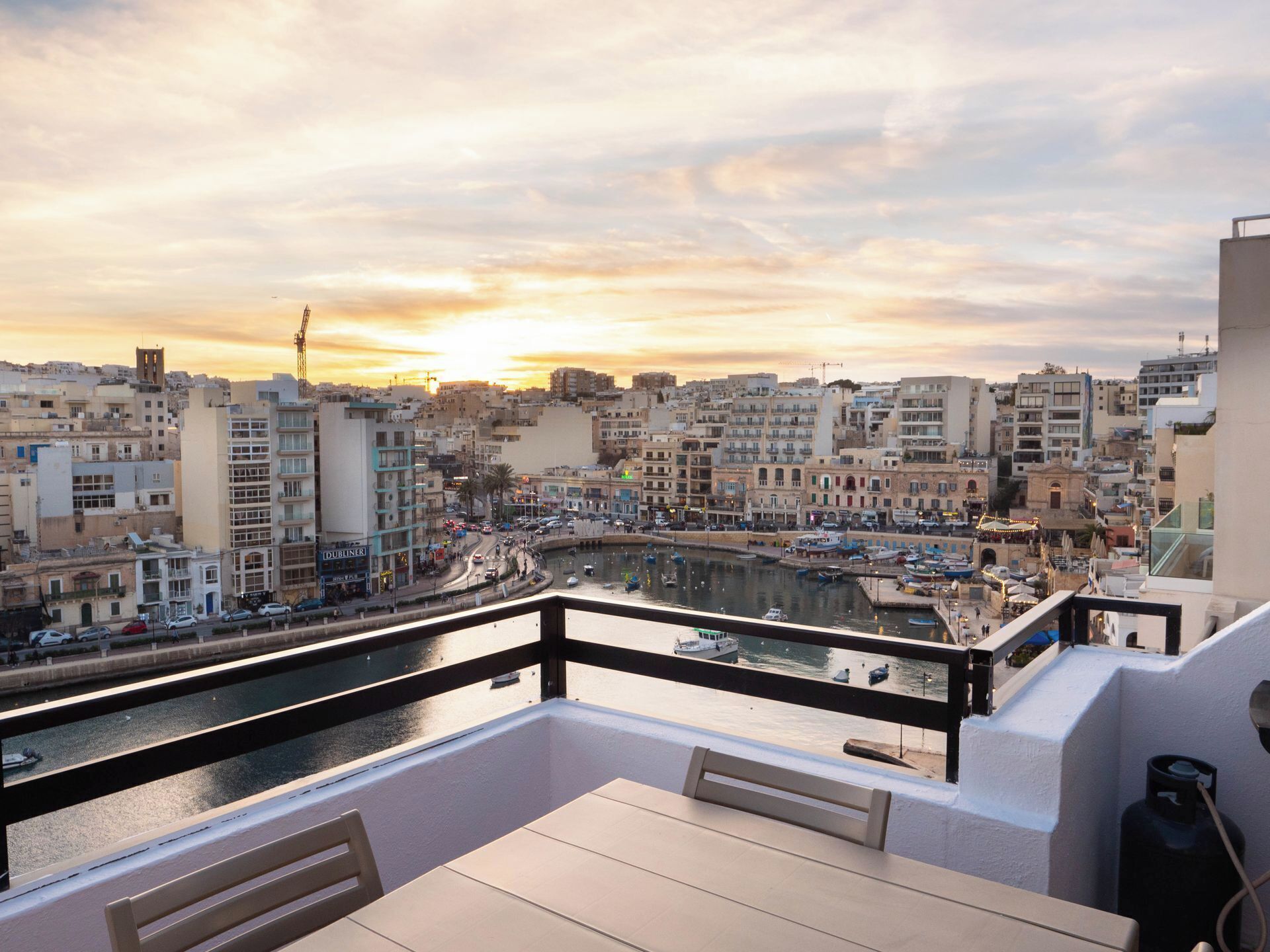 Ein Balkon mit Blick auf eine Skyline im Abendlicht, mit einer Marina und Booten sowie einer belebten Straße.