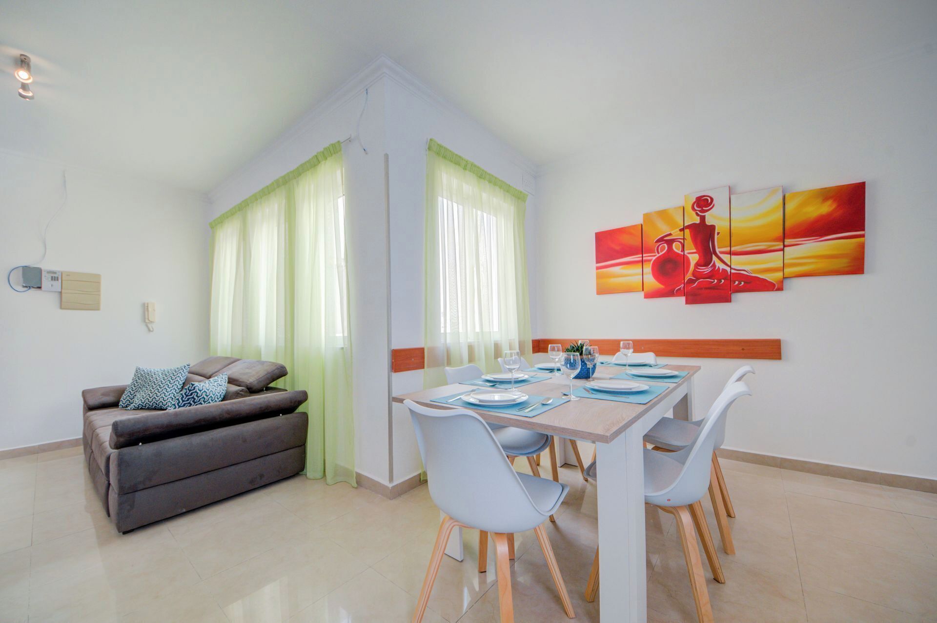 A dining area with a table set for four, a sofa, and a painting on the wall.