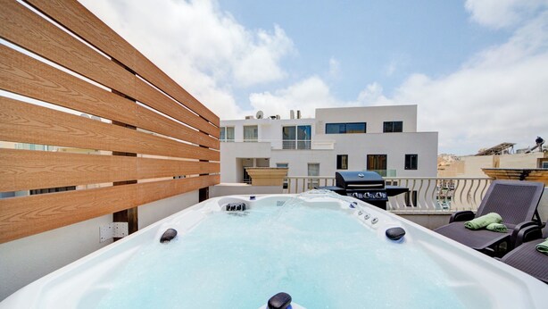 A rooftop with a hot tub, lounge chairs, and a modern building in the background. - Airy Top Floor Apartment With Stunning Terrace (St. Julian's)