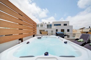 A rooftop with a hot tub, lounge chairs, and a modern building in the background. - Airy Top Floor Apartment With Stunning Terrace (St. Julian's)