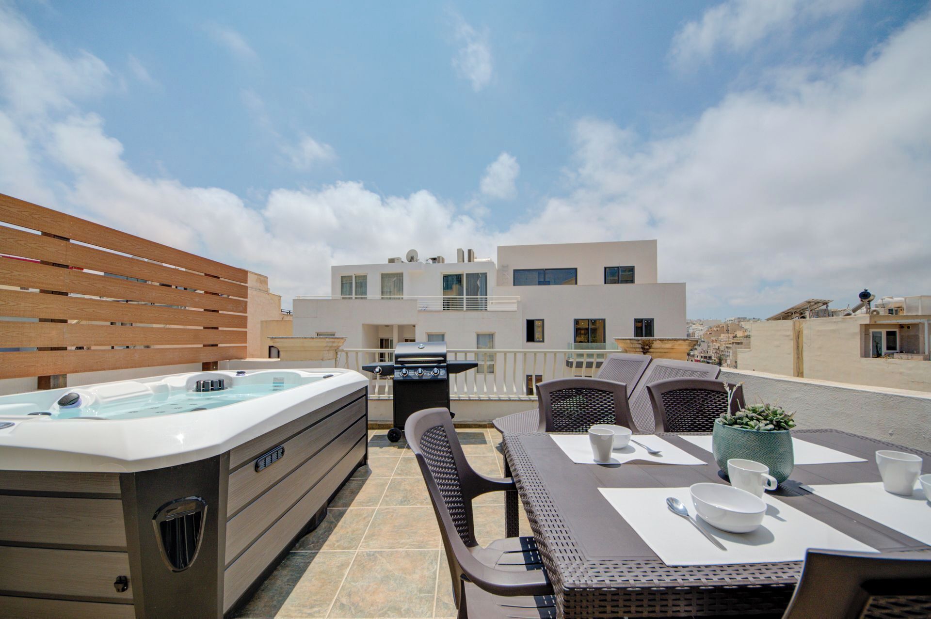 Eine Dachterrasse mit Whirlpool, Sitzgelegenheiten im Freien und Blick auf moderne Gebäude.