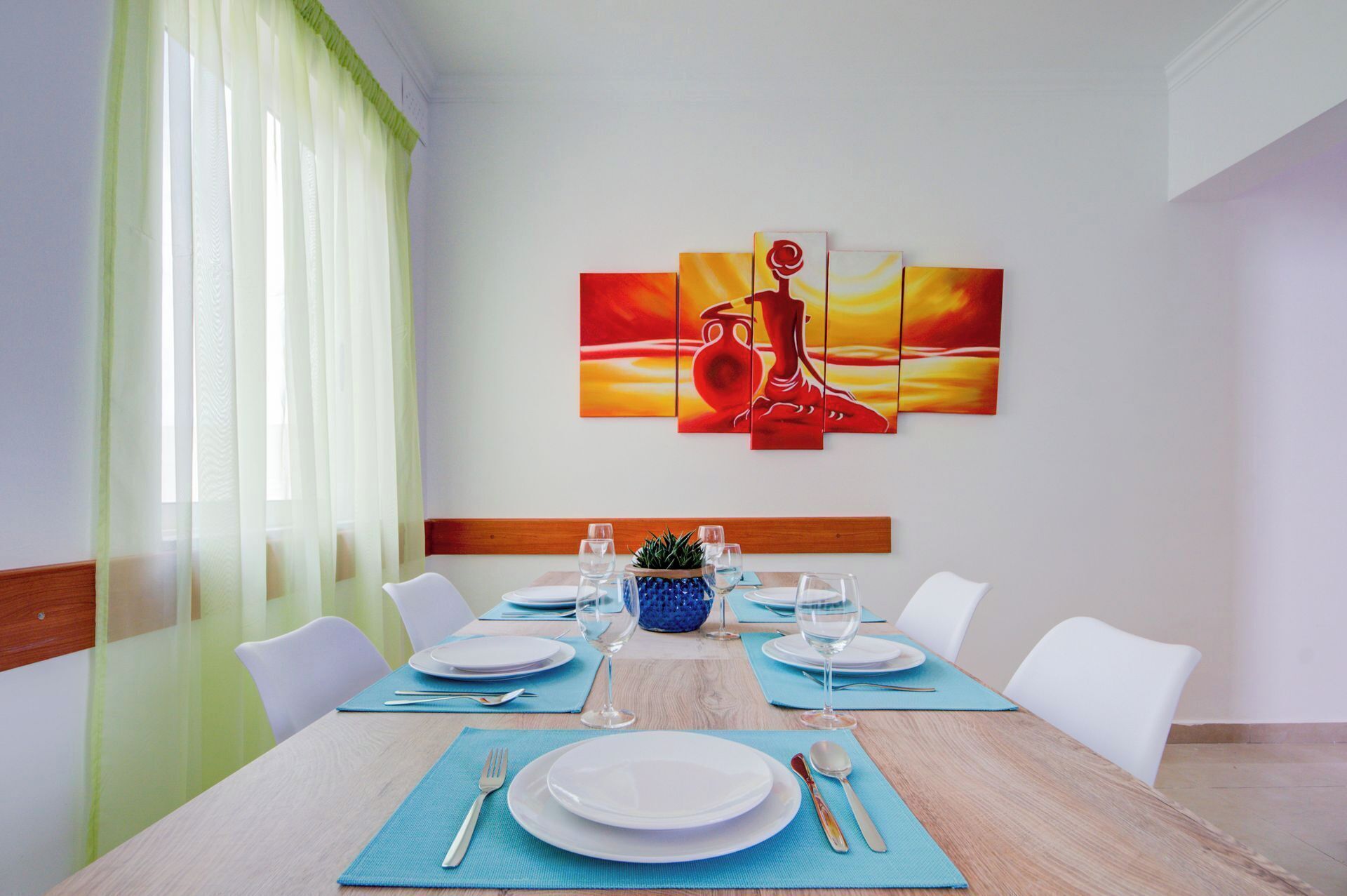 A dining room with a wooden table set for six, white chairs, and a large abstract painting on the wall.