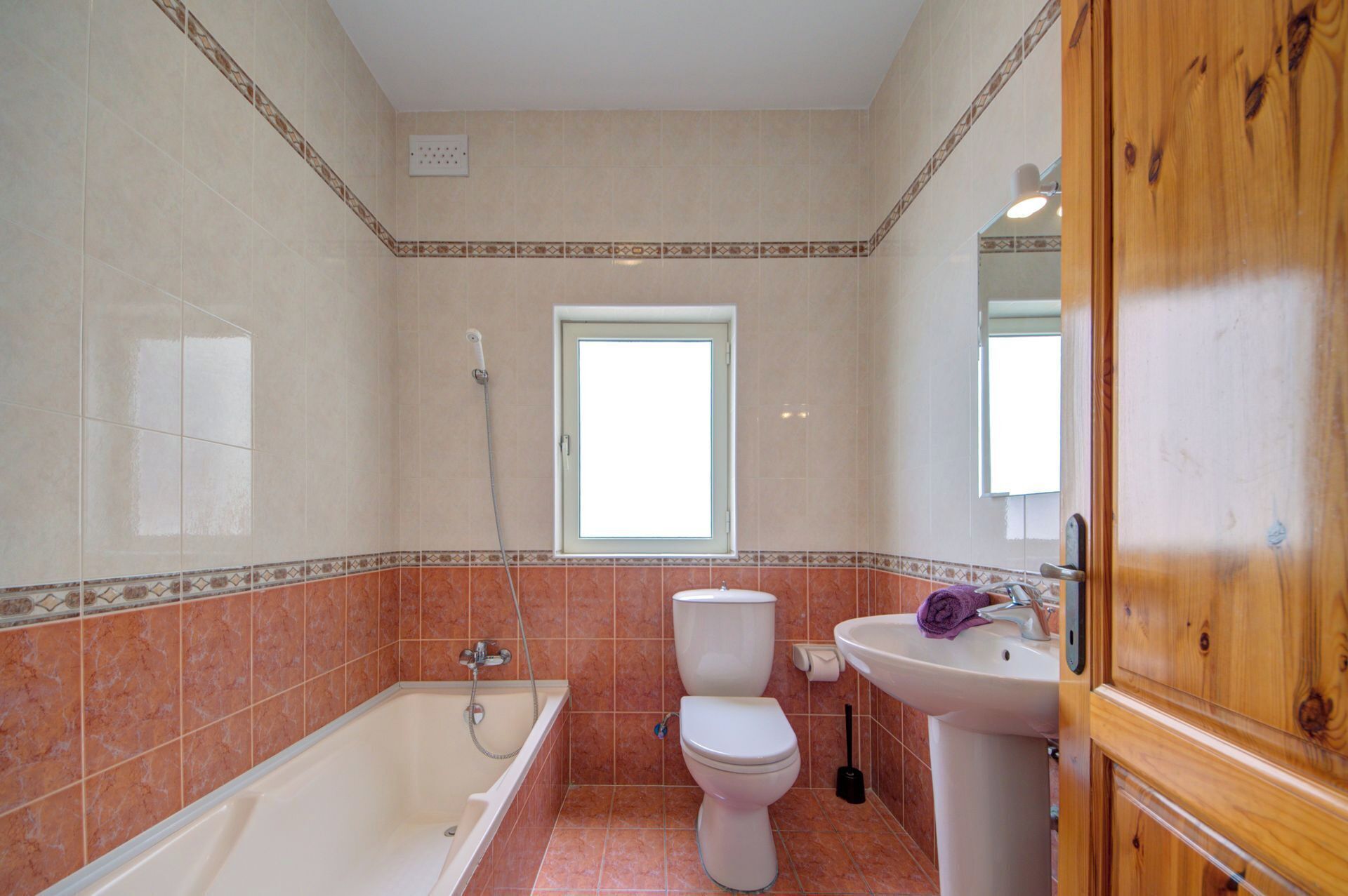 A bathroom with a bathtub, toilet, and sink, featuring a window and patterned tiles.