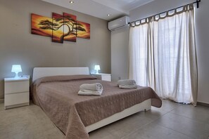 Un dormitorio con una cama grande, dos mesitas de noche con lámparas, un aire acondicionado instalado en la pared y un ventanal con cortinas.