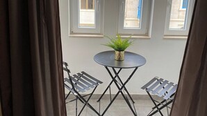 A balcony with two metal chairs, a small round table with a potted plant, and three windows with curtains. - Off the Strand Gzira 3-bedroom Apartment (Gzira)