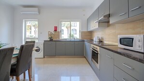 A modern kitchen with grey cabinets, a built-in oven, and a microwave. There is a window with a view of palm trees and a building outside. - Magnificent Minimal Apartment Close to Attractions (St. Julian's)